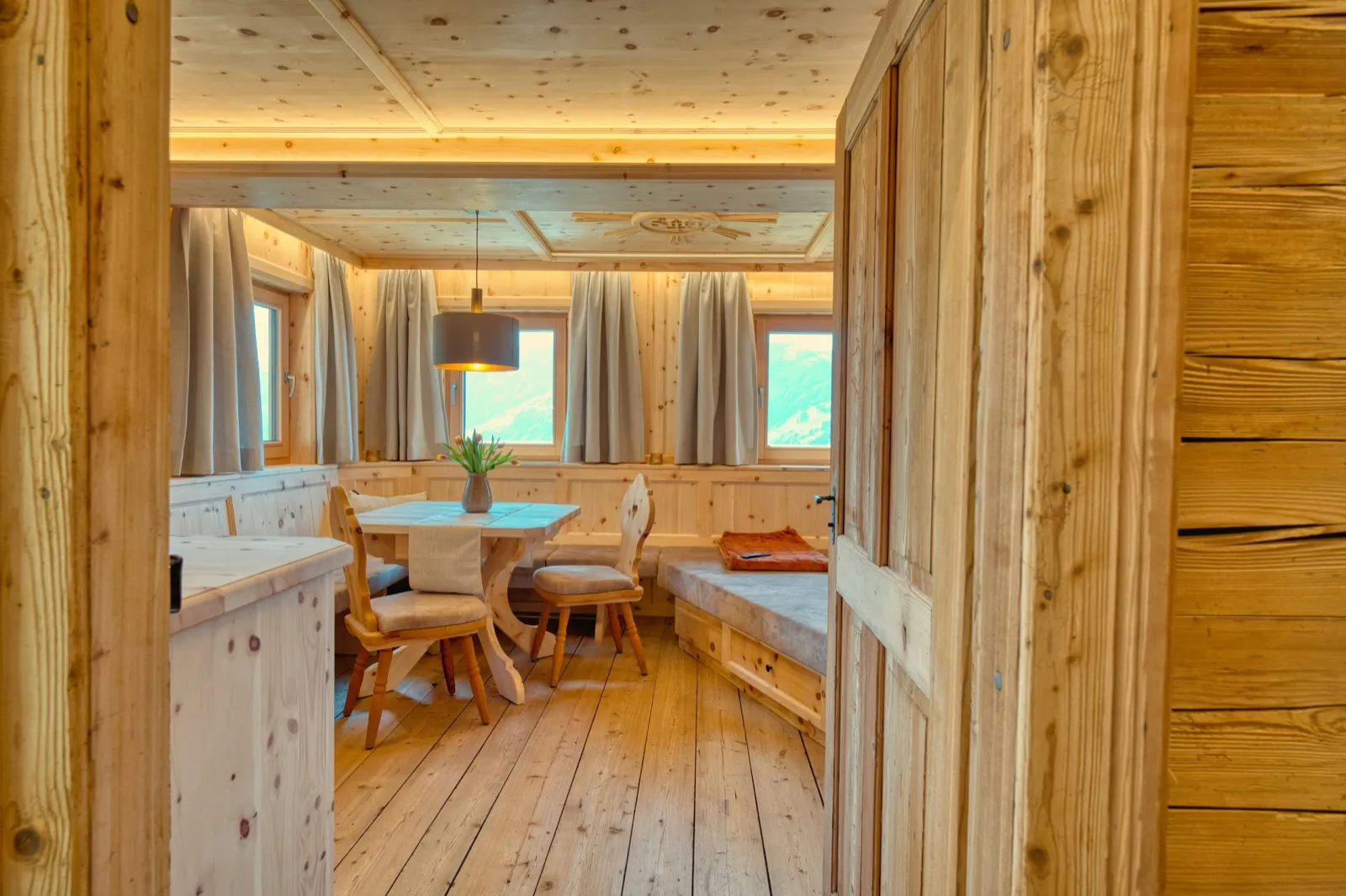 Warm wood-panelled ski chalet interior with a dining nook and windows looking out to the mountains